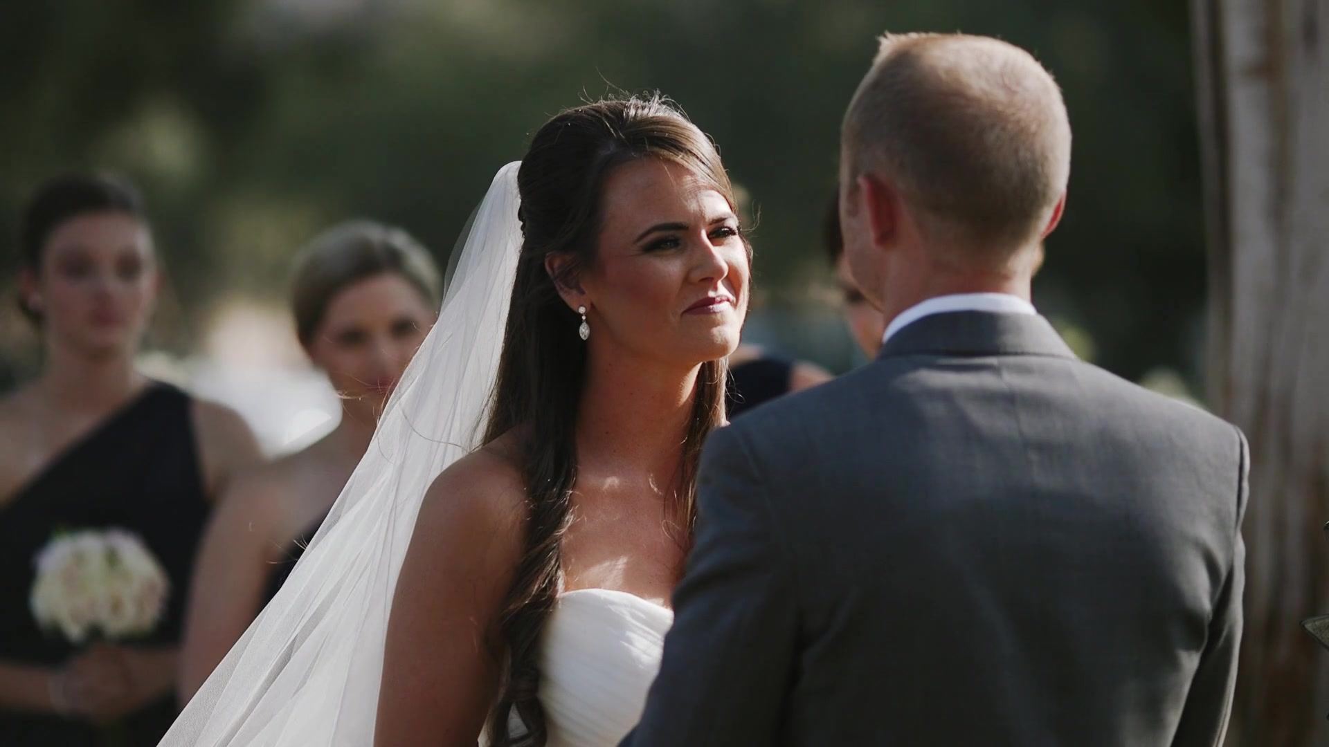 Jade looking up at Josh during the vows, her veil catching the light, a bridesmaid in navy behind her.
