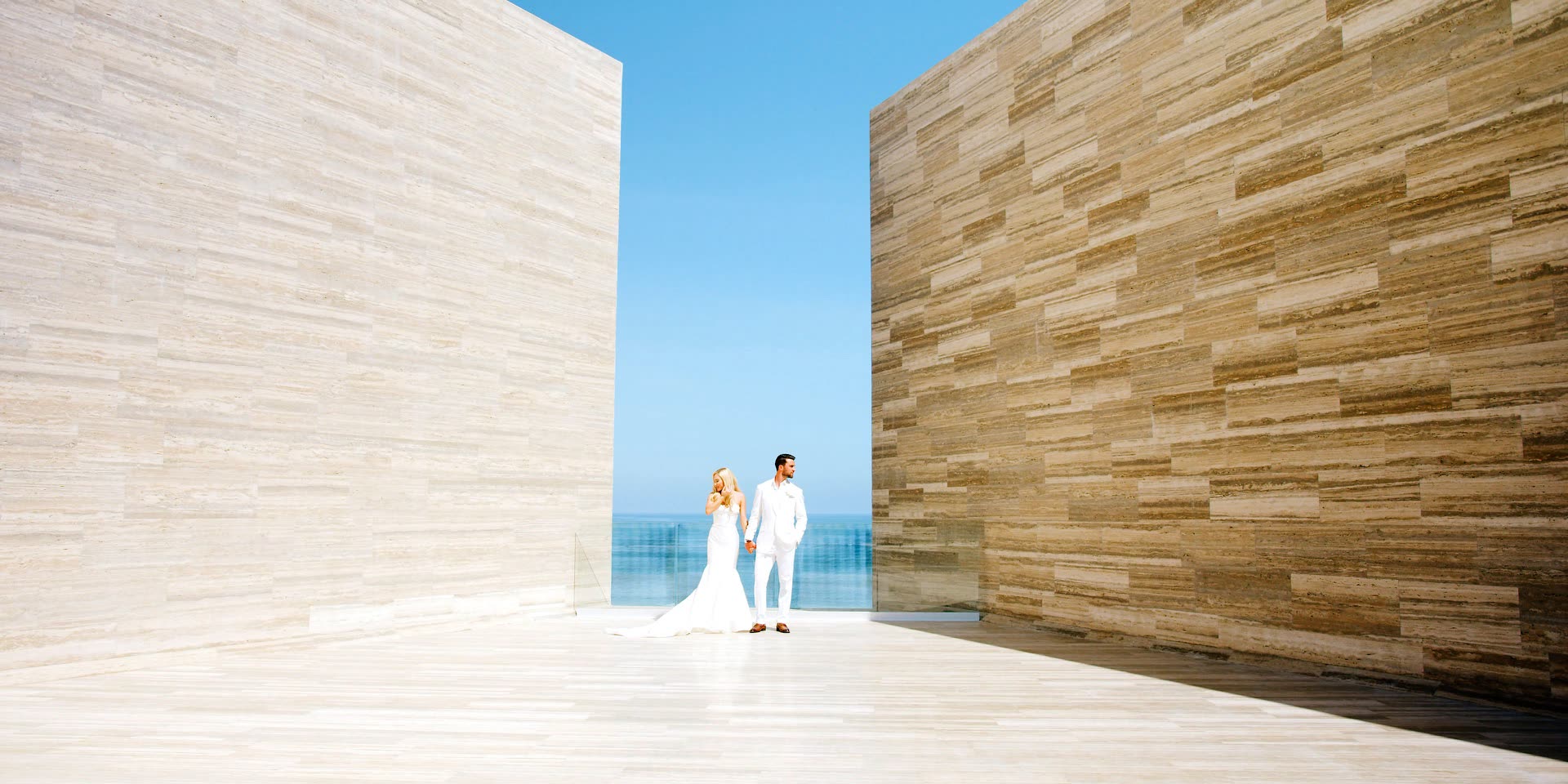 Bride and groom between the travertine walls of a San Jose del Cabo resort with the Sea of Cortez beyond