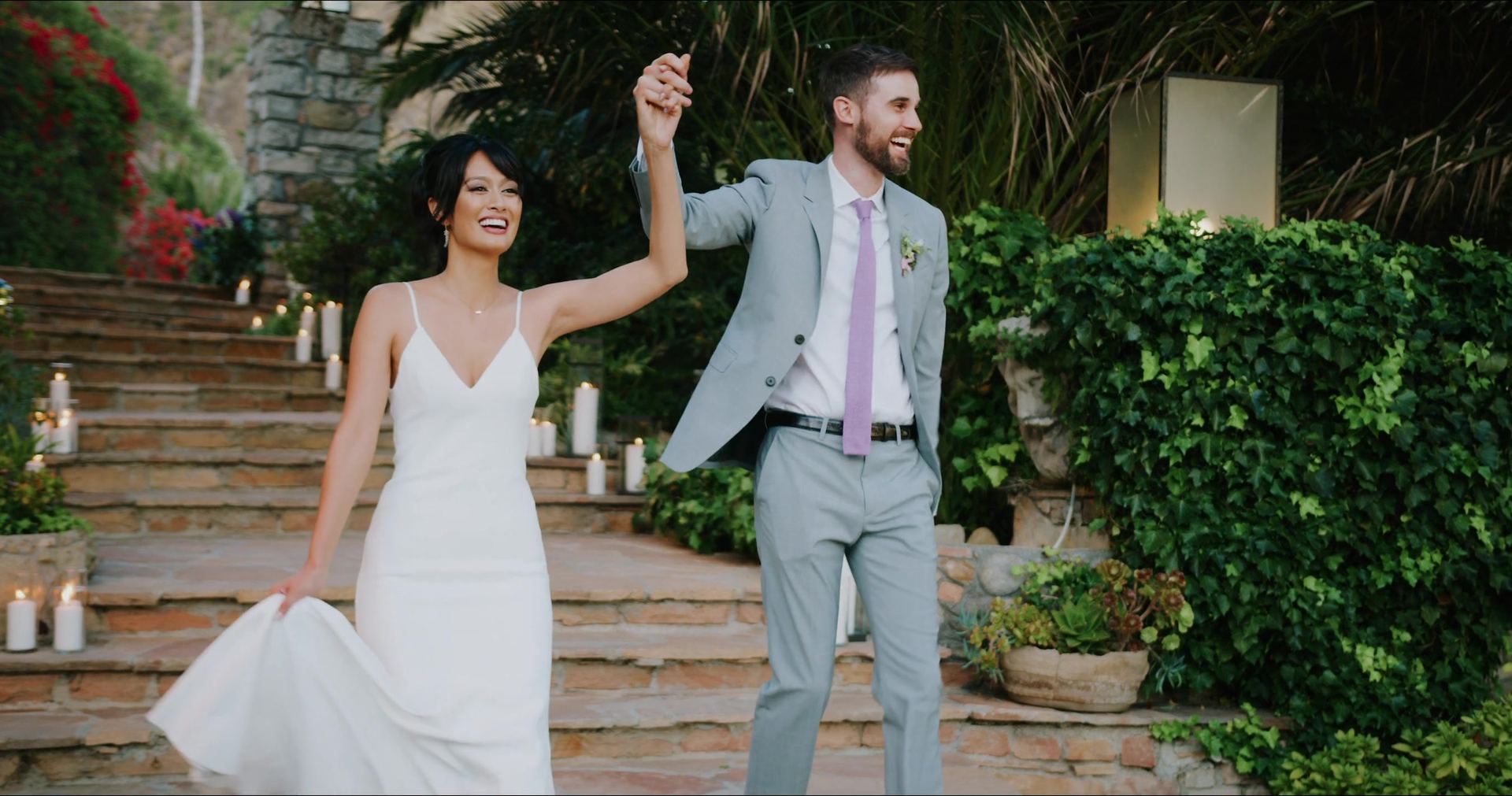 James and Katrina coming down the candlelit steps with their joined hands raised, bougainvillea spilling over the wall behind them.