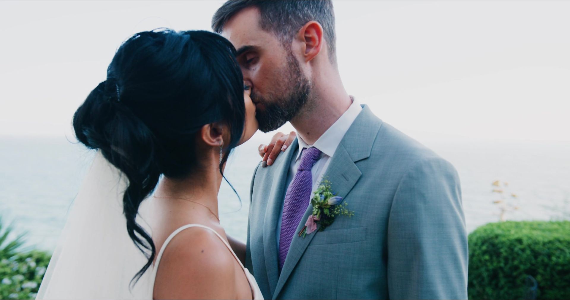 James kissing Katrina's forehead above the water, the ocean flat and pale behind them.