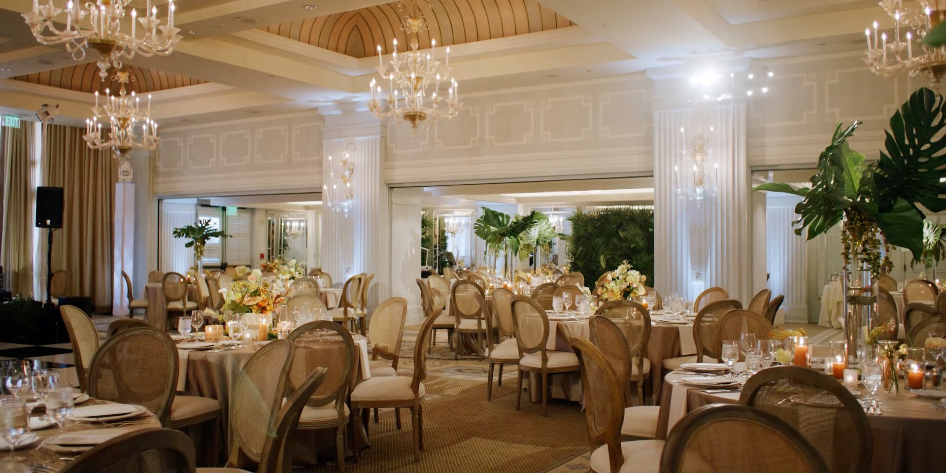 Hotel Casa Del Mar ballroom set for a wedding reception, cane chairs and chandeliers with tropical greenery