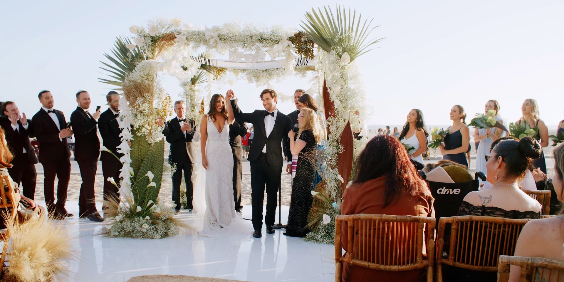 Beach wedding ceremony on the sand at Hotel Casa Del Mar, the couple raising their hands beneath the floral arch