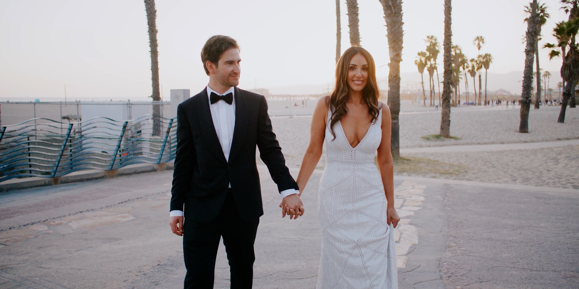 Bride and groom walking the Santa Monica beach promenade at sunset near Hotel Casa Del Mar