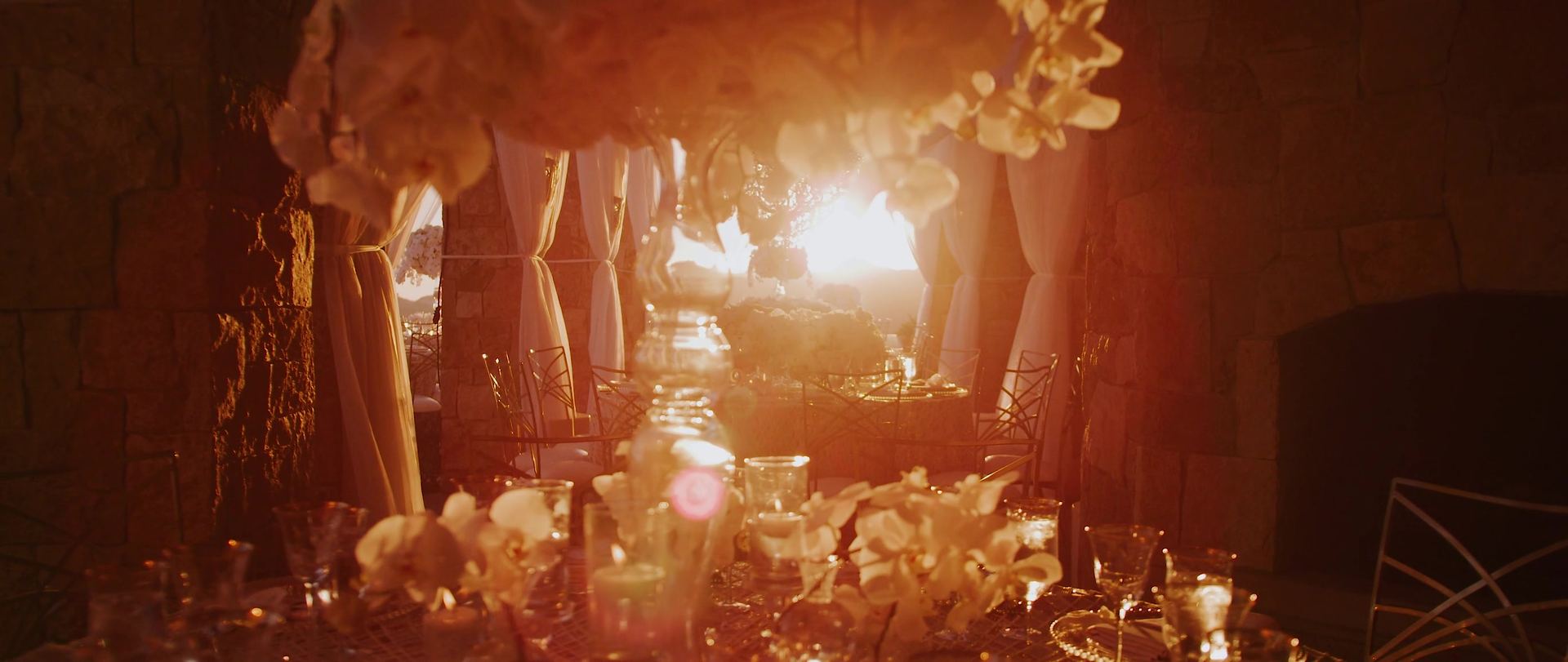 Candlelight and white blooms along the reception table at Malibu Rocky Oaks, low sun flaring through the drapes behind.