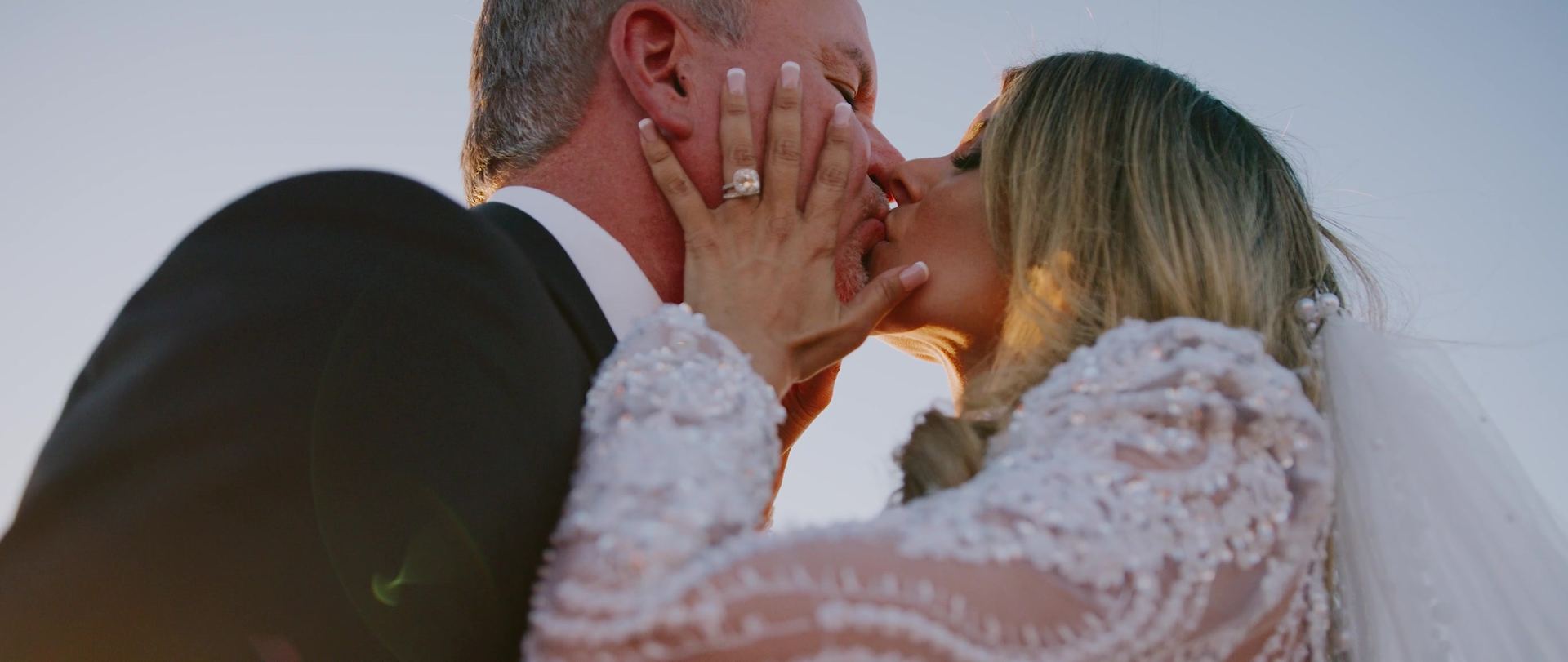 Michele's hands framing Jeff's face as they kiss, her ring and the beadwork along her sleeve close in the frame.