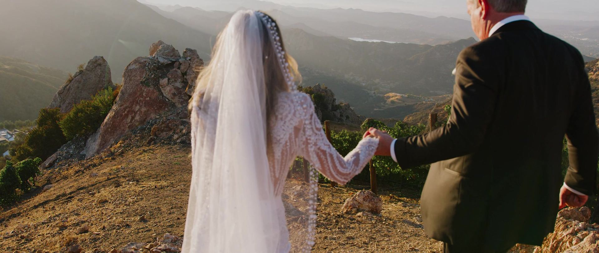 Jeff and Michele holding hands as they cross the rocky ridge at Malibu Rocky Oaks, her veil running the full length of her back.