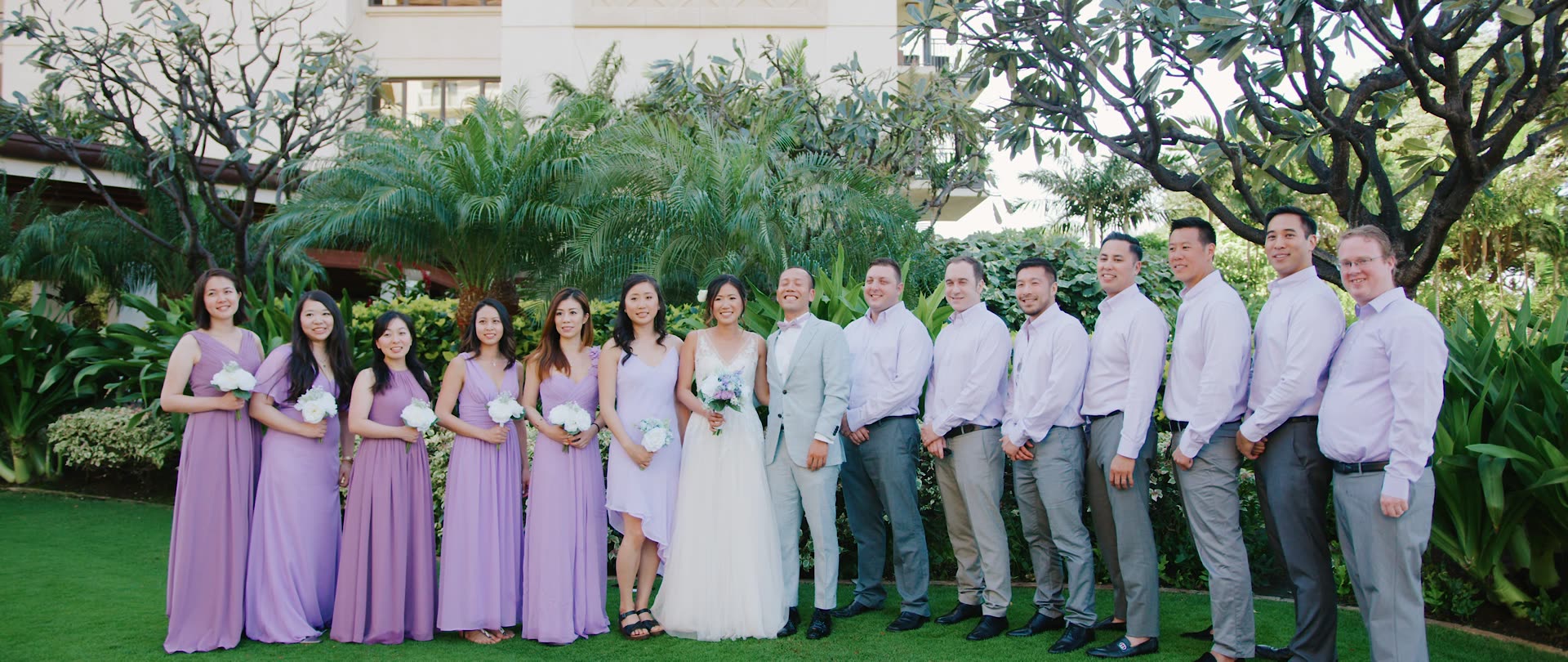 A wedding party in lavender on the Ocean Gardens lawn beneath the plumeria trees