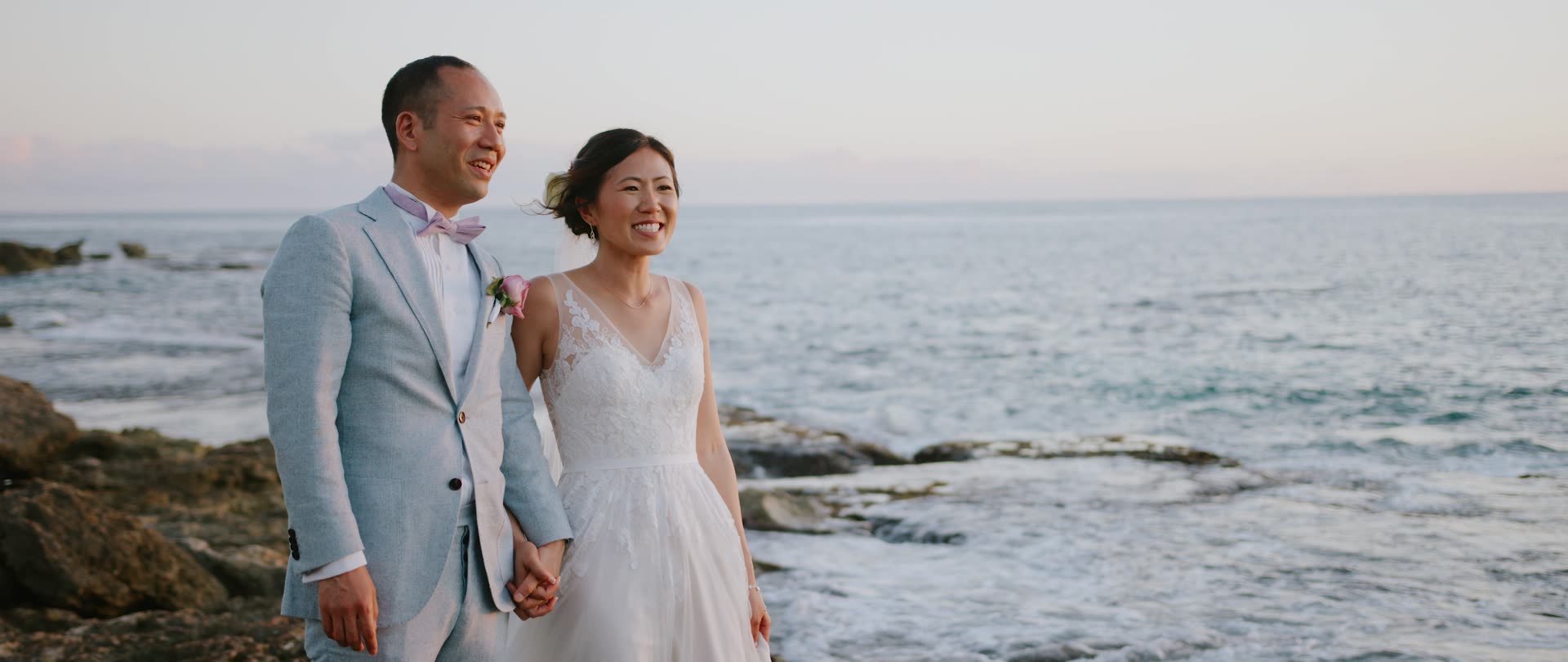 A bride and groom walking the volcanic rock shelf at the water's edge at Paradise Cove, Oahu