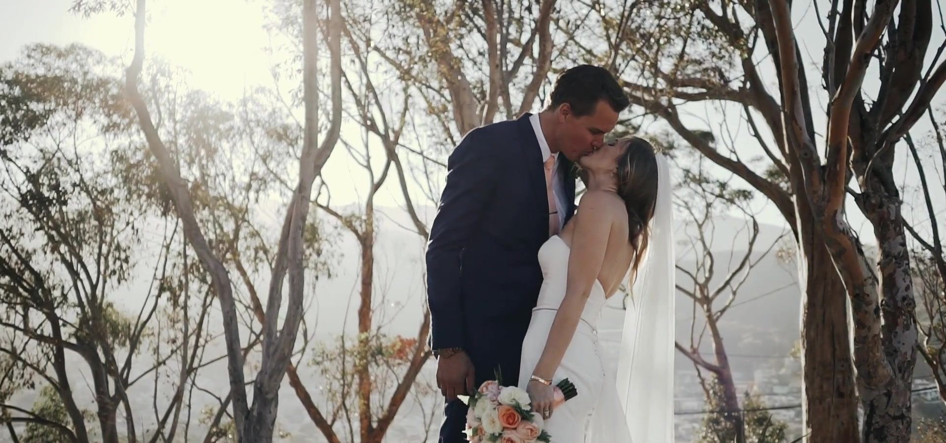 Kyle kissing Ava under the eucalyptus, the sun low behind the branches, her bouquet at her side.