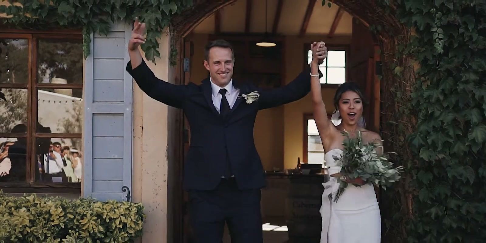 Keshiia and Kevin cheering in the doorway of an ivy-covered building, a blue shutter beside them.