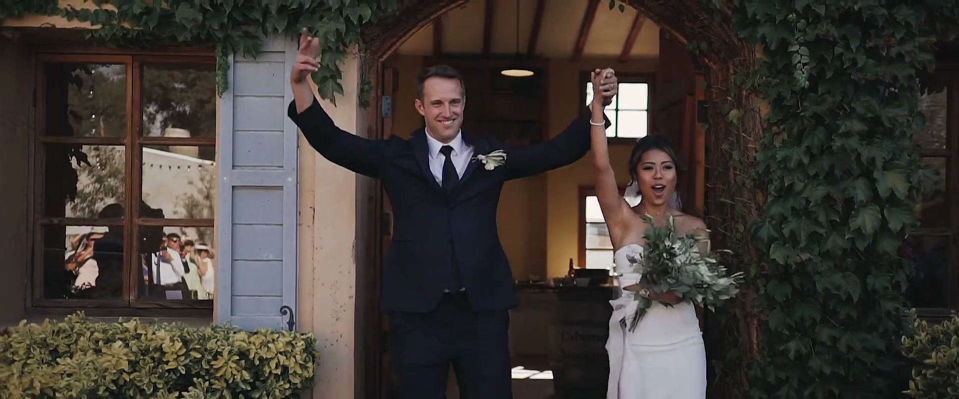 Keshiia and Kevin with their arms raised in the doorway of an ivy-covered building