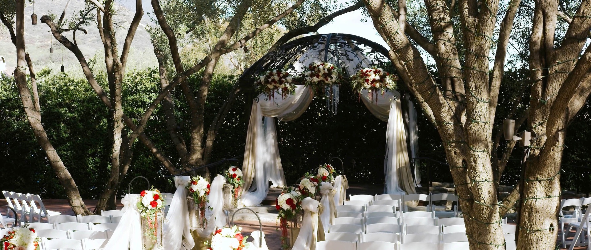 Padua Hills Theatre garden ceremony with a wrought-iron arch and florals set beneath the olive trees with mountain views