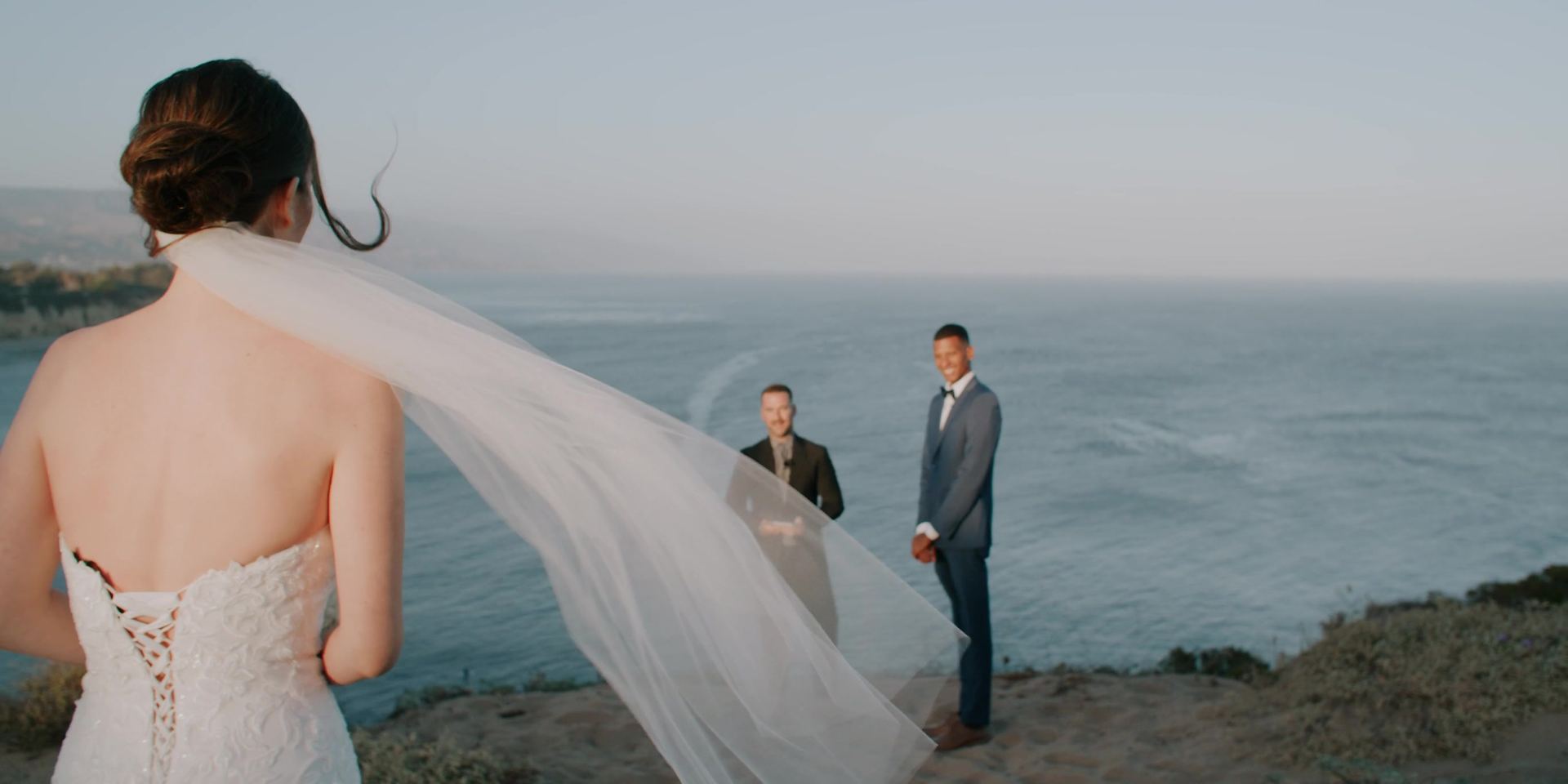 Lindsey walking toward Lucas and the officiant on the bluff, her veil lifting behind her.