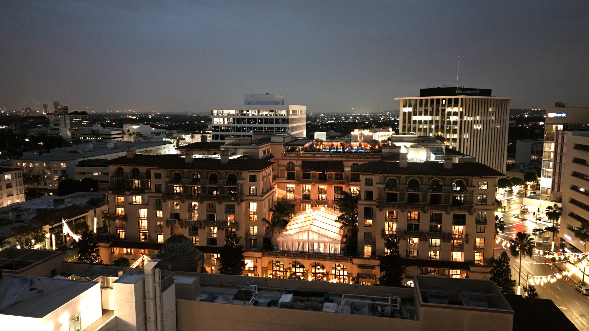 The Maybourne Beverly Hills at night, its lit facade and glass-roofed terrace pavilion set against the Beverly Hills skyline