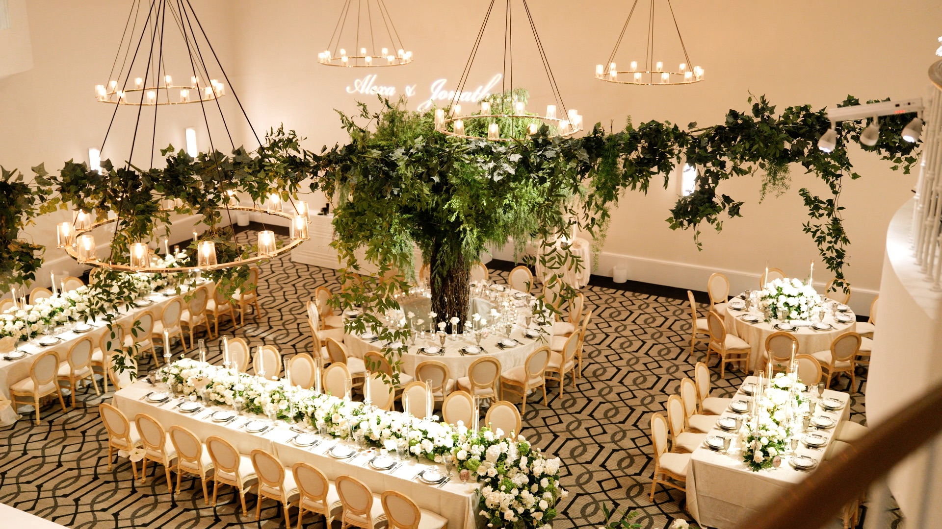 The Maybourne Beverly Hills ballroom set for a wedding reception, ring chandeliers and hanging greenery above long banquet tables