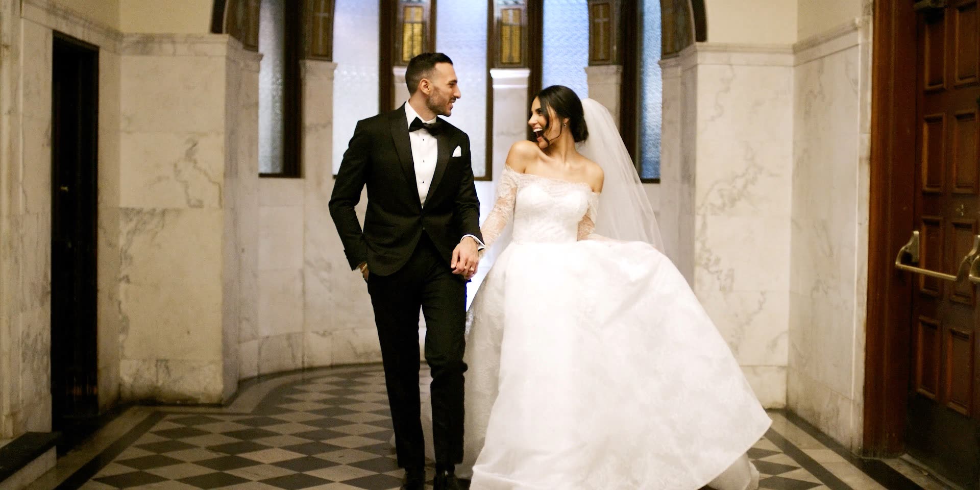 Bride and groom walking the marble corridor at Vibiana, checkered floor and stained glass
