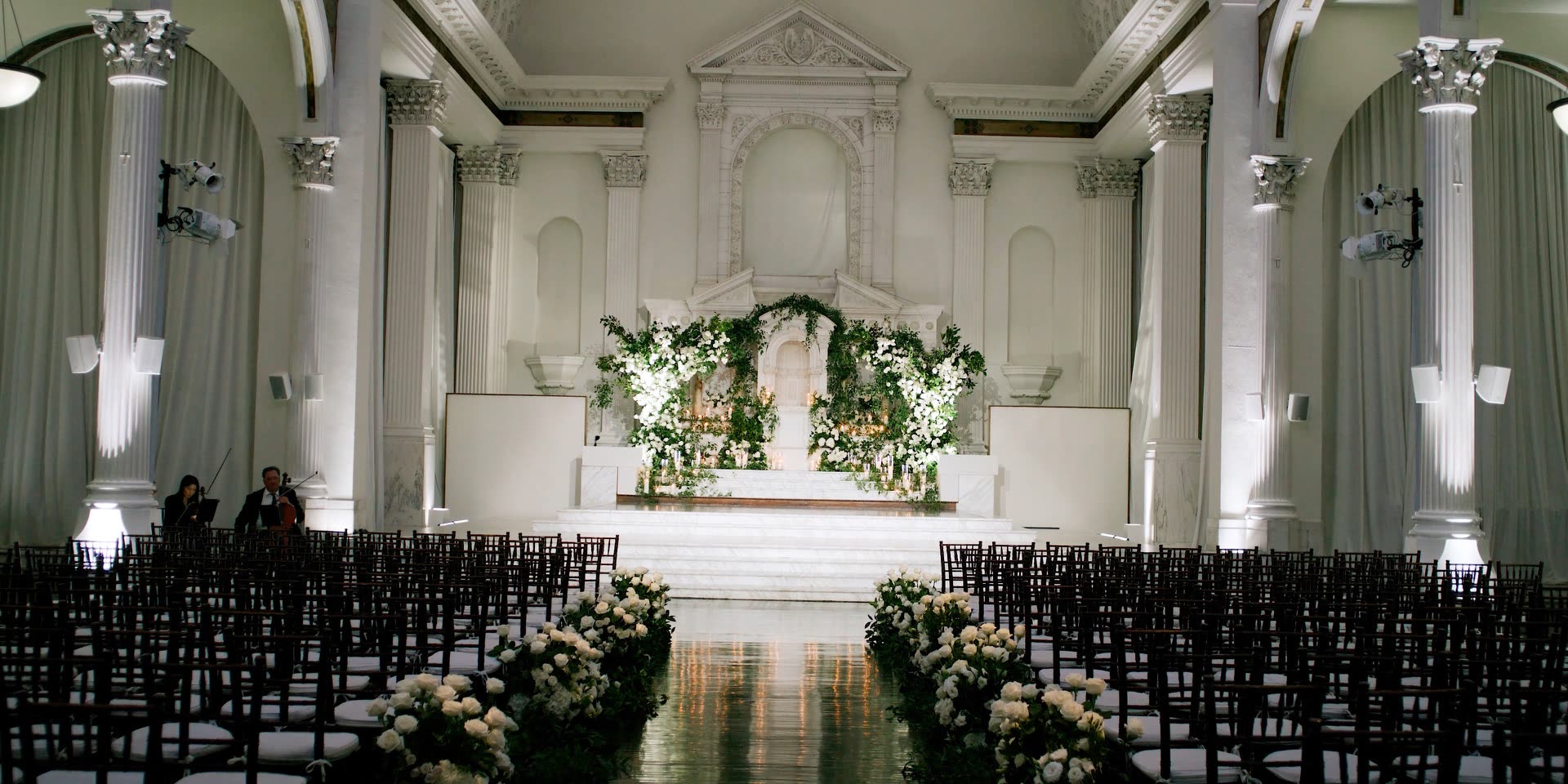 The Vibiana nave set for a wedding ceremony, dark chiavari chairs and a white floral altar beneath the vaulted ceiling