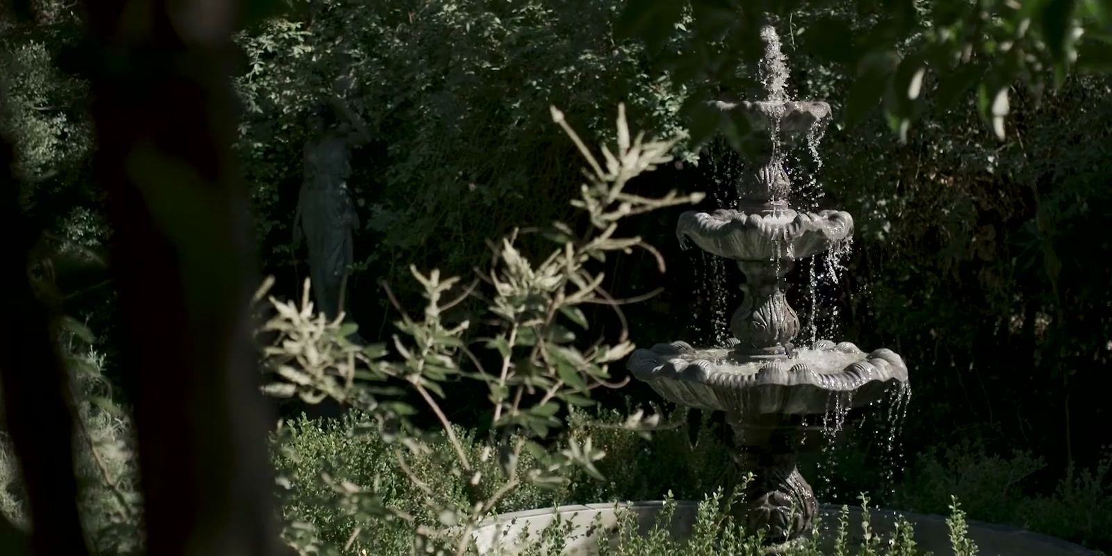 A tiered stone fountain among dark green planting in the garden.