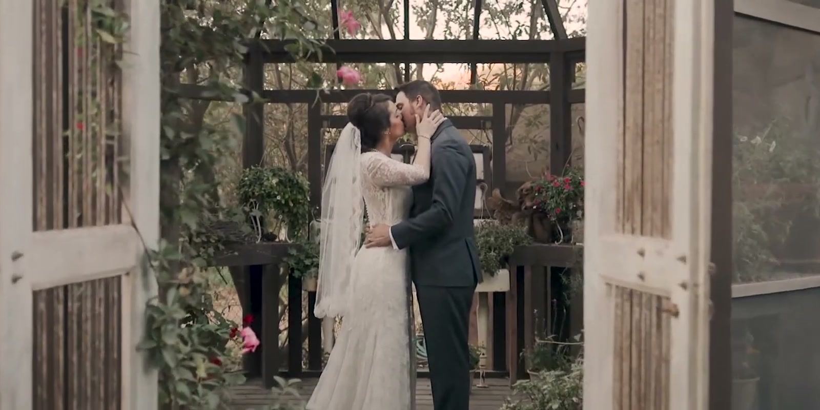 Nick and Danielle kissing inside a rustic atrium, its weathered white doors open in the foreground.
