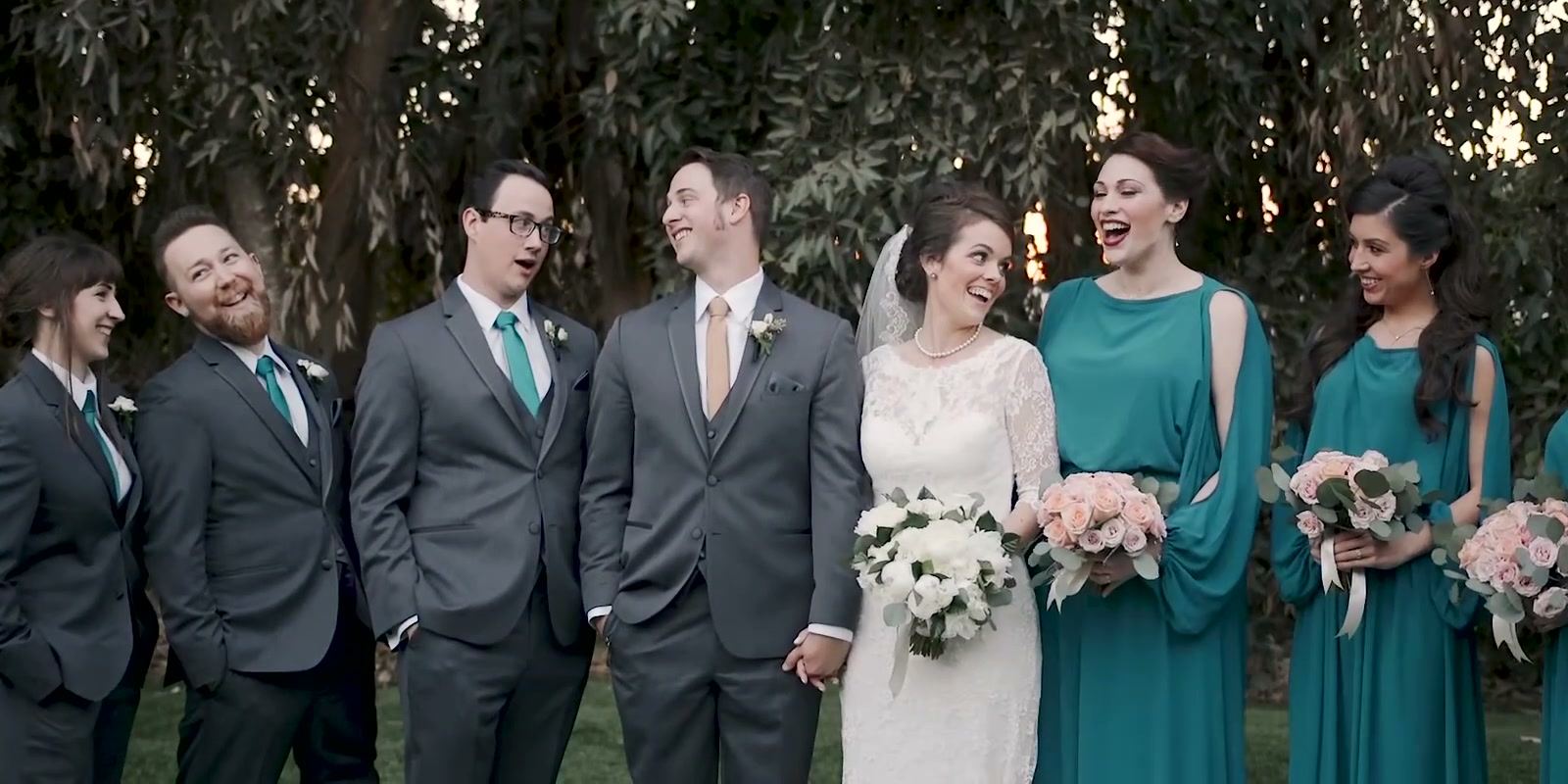 Nick and Danielle laughing with their wedding party on the lawn, bridesmaids in teal and groomsmen in grey.