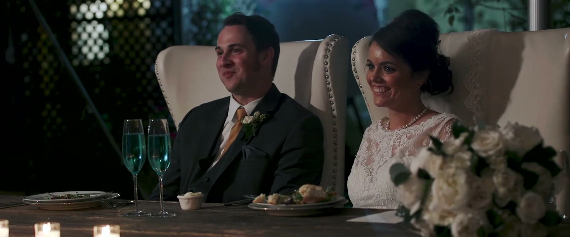 Nick and Danielle laughing at their head table in tall white chairs, blue drinks in front of them.