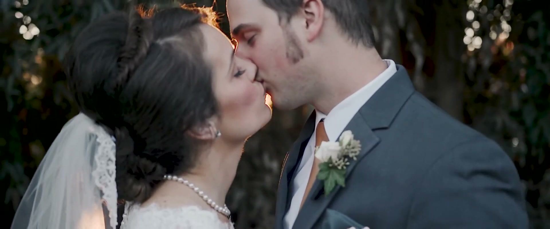 Danielle and Nick kissing in the garden, his boutonniere of white flowers close in the frame.