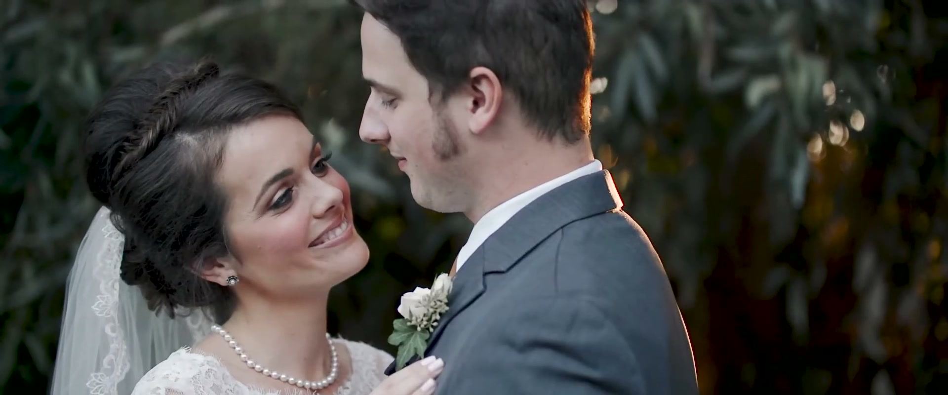 Danielle smiling up at Nick, the two of them close among dark green leaves.