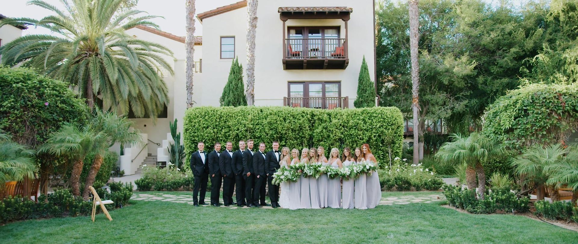 The wedding party on the lawn in front of the Spanish-style building, palms rising behind them.