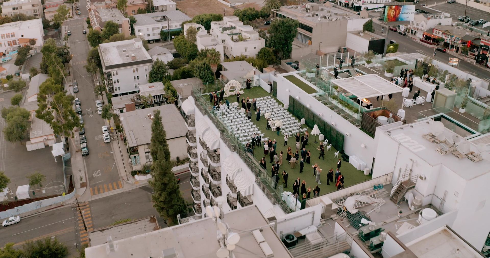 Aerial view of the hotel rooftop, the ceremony lawn and pool deck set out among the surrounding streets.
