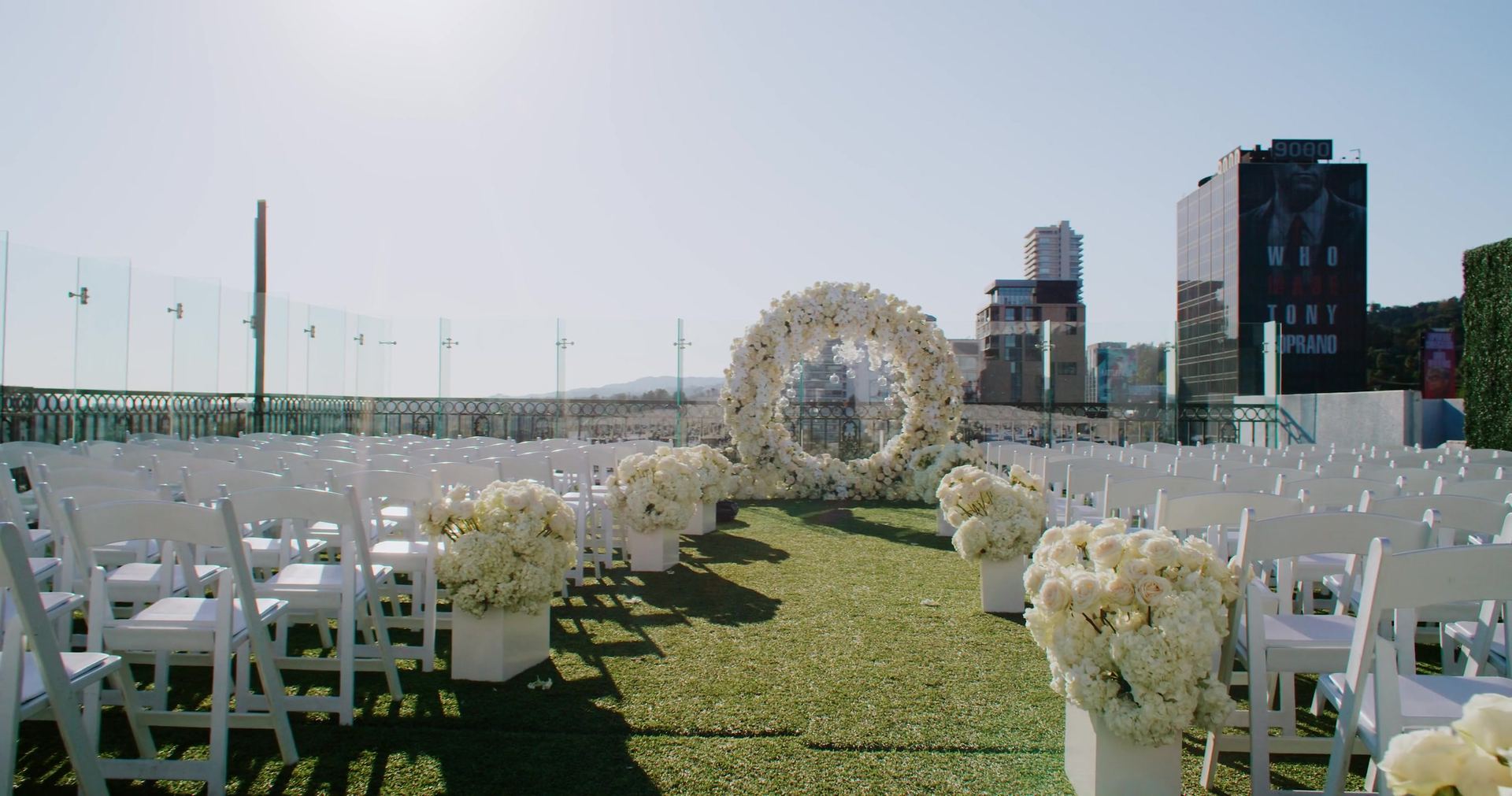 The rooftop ceremony set at The London West Hollywood, a circular arch of white blooms on the lawn with rows of white chairs and the city beyond.