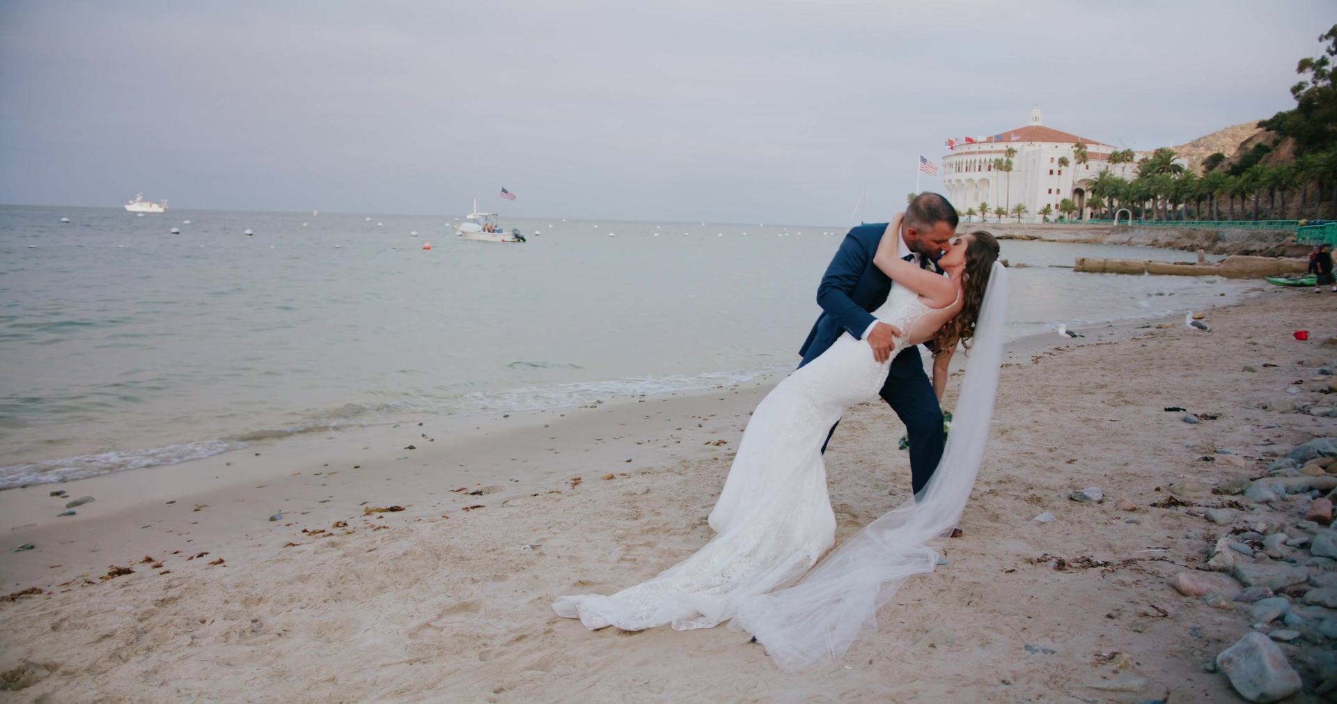 Timothy dipping Amber for a kiss on the sand, the Casino building behind them.