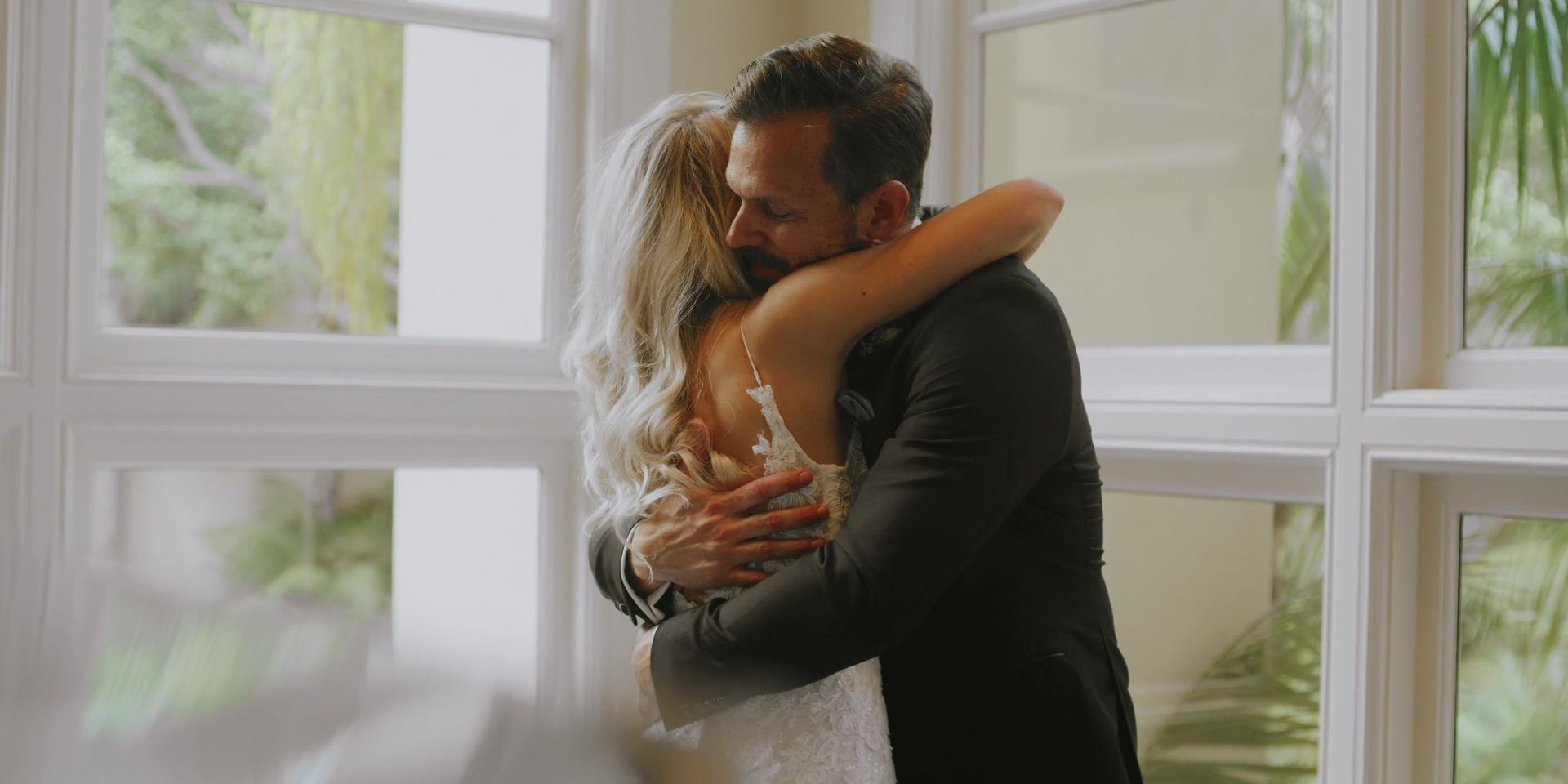 Tony holding Katherine in a long embrace in front of the windows, her lace gown against his dark suit.