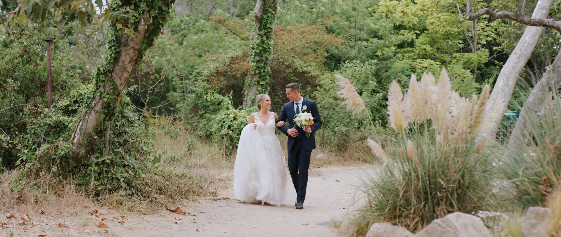 Teddy and Lindsay walking a path lined with pampas grass.