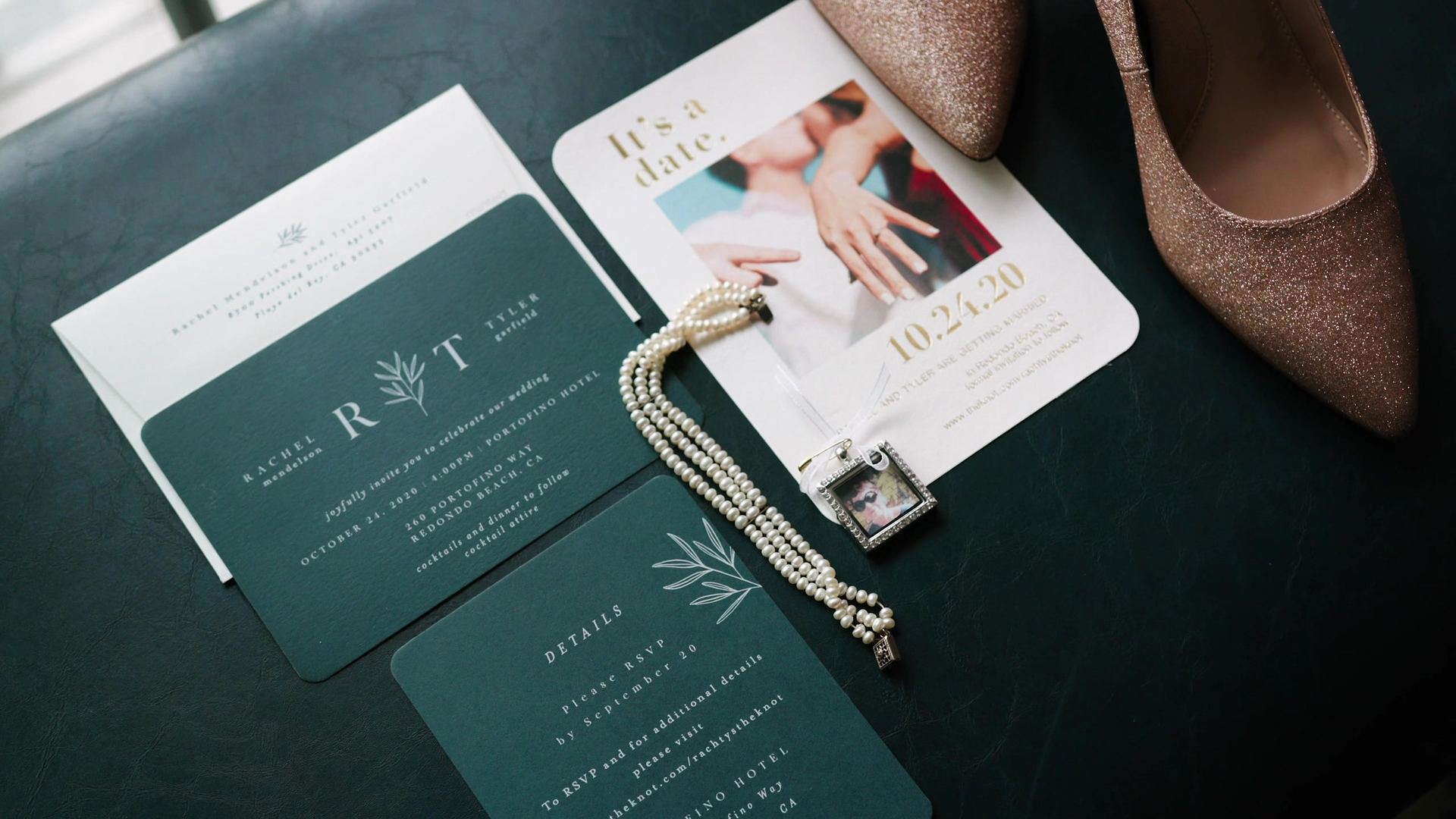 The invitation suite laid out in deep green beside the bride's shoes and a string of pearls.